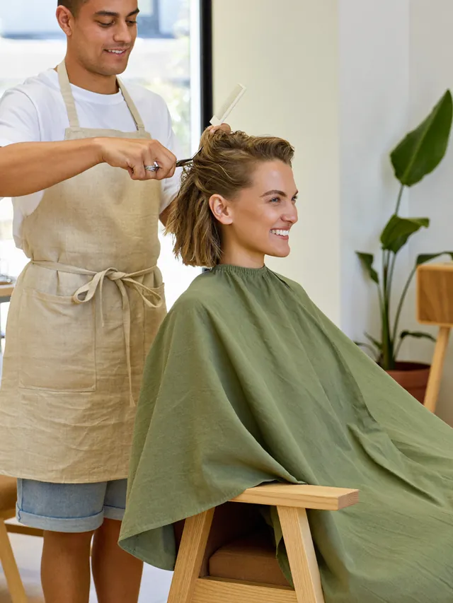 A stylist trimming a smiling client’s hair in the studio